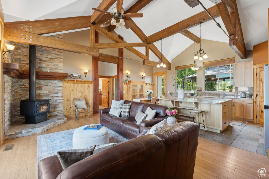 Living room with a wood stove, beamed ceiling, light hardwood / wood-style flooring, and high vaulted ceiling