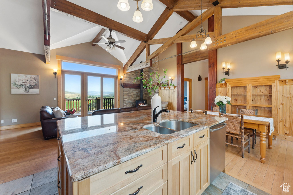 Kitchen with light wood-type flooring, an island with sink, ceiling fan, light stone countertops, and sink