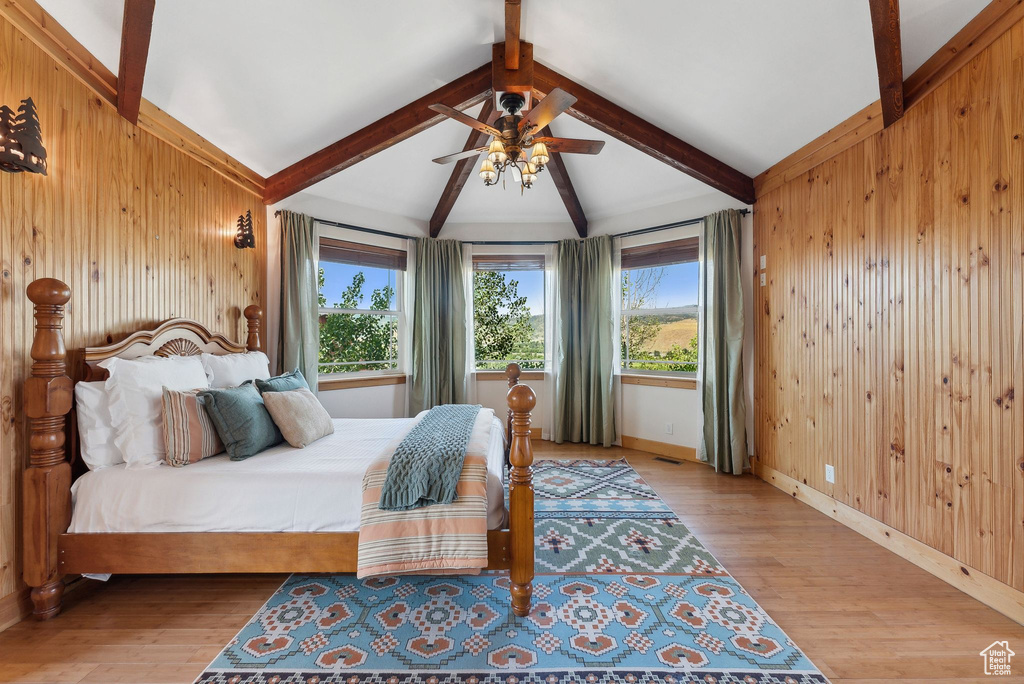 Bedroom featuring wood walls, light hardwood / wood-style flooring, lofted ceiling with beams, and ceiling fan