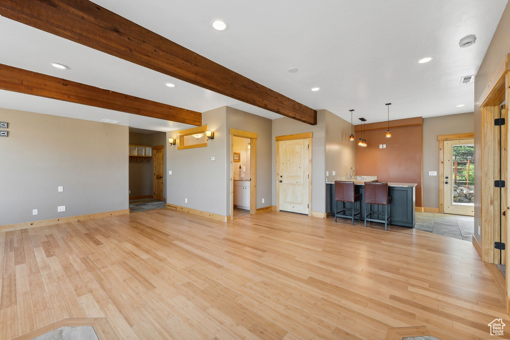 Unfurnished living room featuring sink, light hardwood / wood-style flooring, and beam ceiling