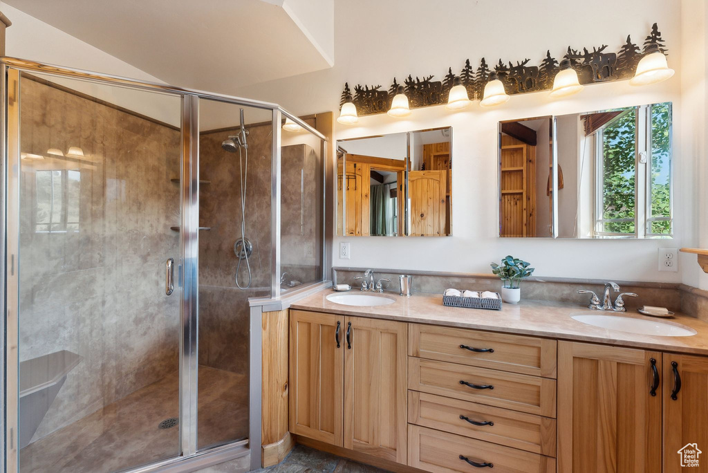 Bathroom featuring dual vanity, a shower with door, and vaulted ceiling