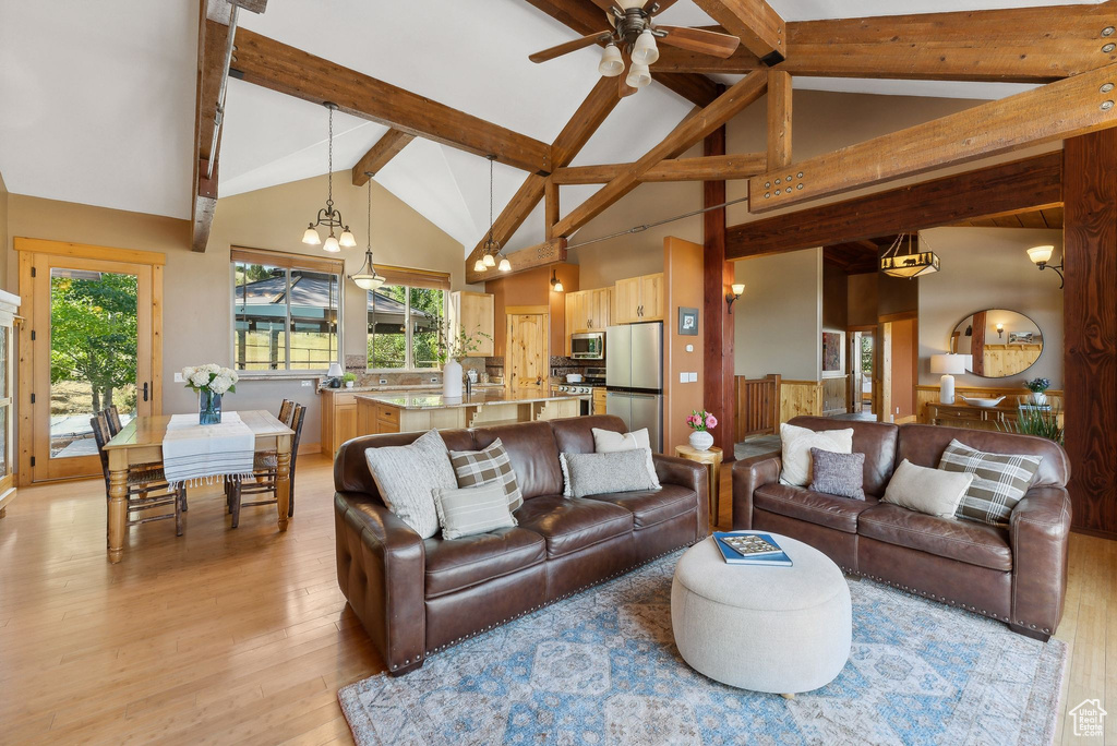 Living room with light hardwood / wood-style flooring, high vaulted ceiling, ceiling fan with notable chandelier, and plenty of natural light