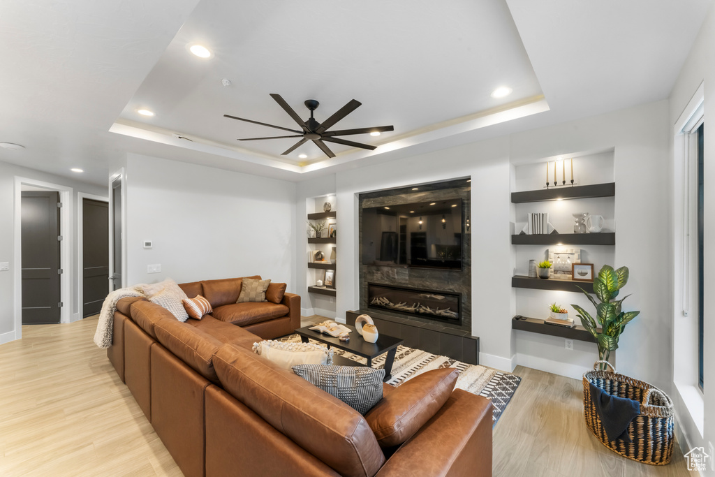 Living room with a tile fireplace, ceiling fan, light wood-type flooring, and a tray ceiling