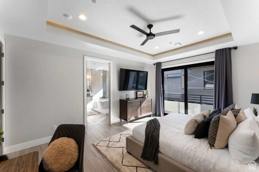 Bedroom featuring connected bathroom, access to exterior, ceiling fan, a tray ceiling, and wood-type flooring