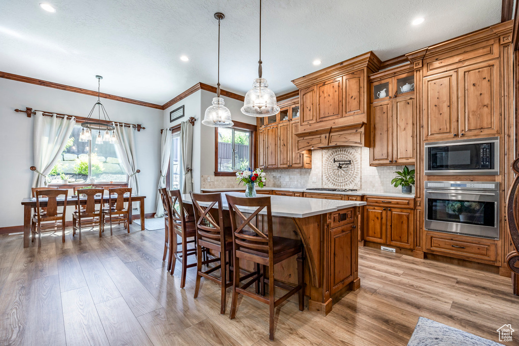 Kitchen with light wood-type flooring, a center island, stainless steel appliances, hanging light fixtures, and decorative backsplash