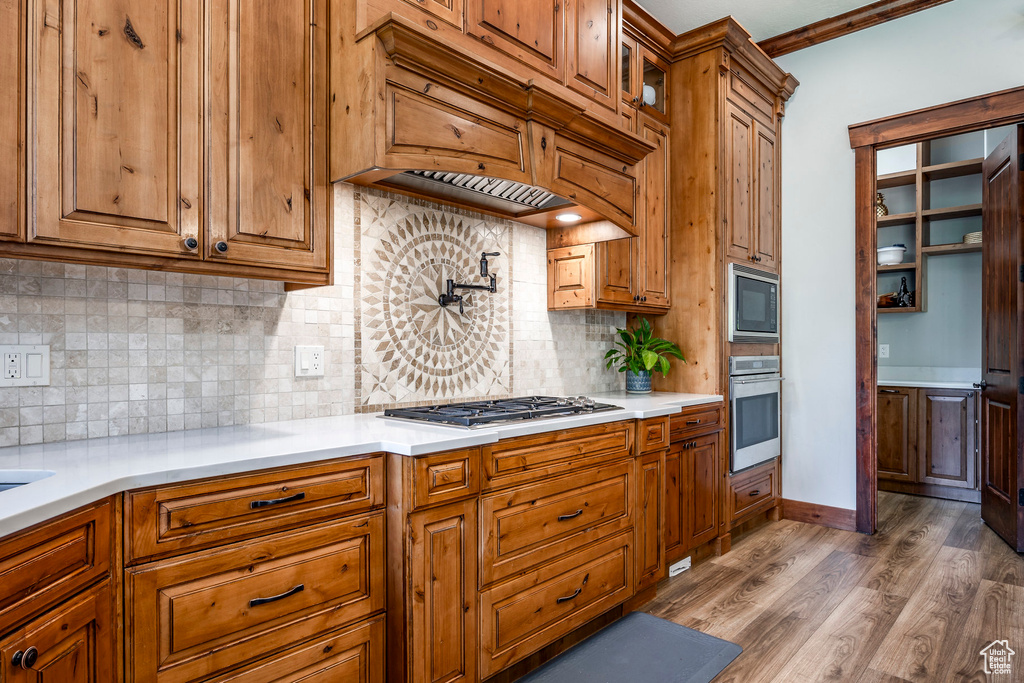 Kitchen featuring stainless steel appliances, decorative backsplash, crown molding, and wood-type flooring