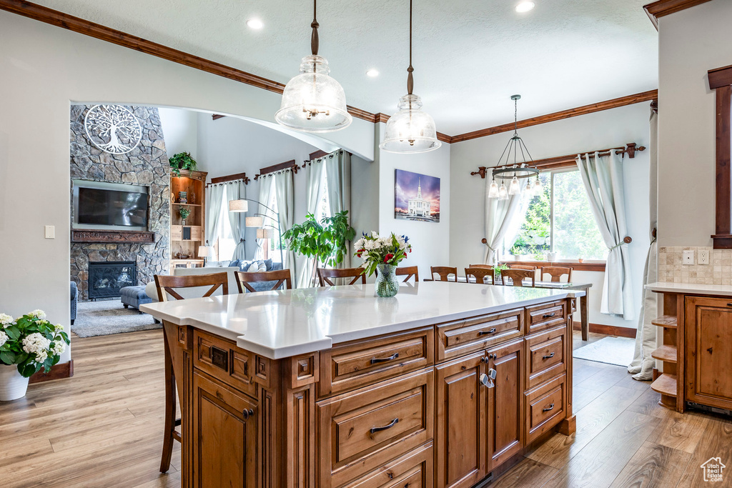 Kitchen with backsplash, a center island, pendant lighting, light hardwood / wood-style floors, and a stone fireplace