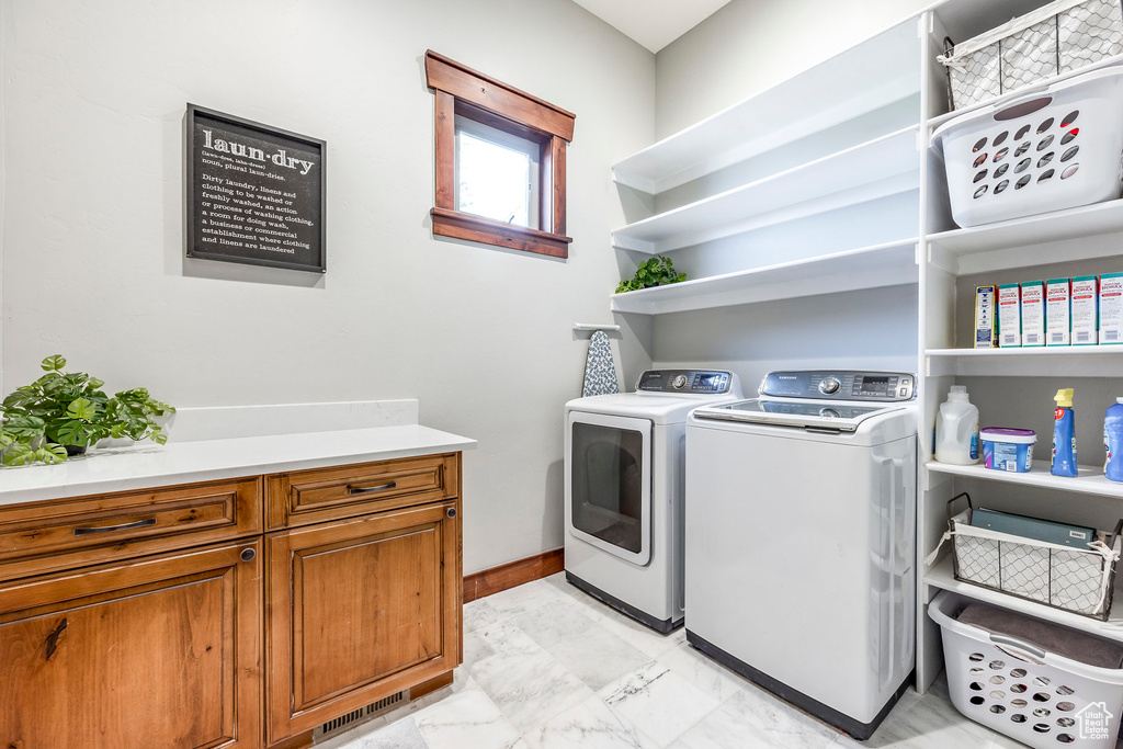 Clothes washing area featuring washing machine and clothes dryer, light tile patterned flooring, and cabinets