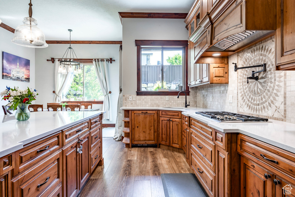 Kitchen featuring tasteful backsplash, pendant lighting, hardwood / wood-style floors, crown molding, and sink