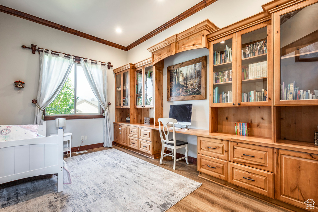 Office featuring crown molding, built in desk, and light wood-type flooring