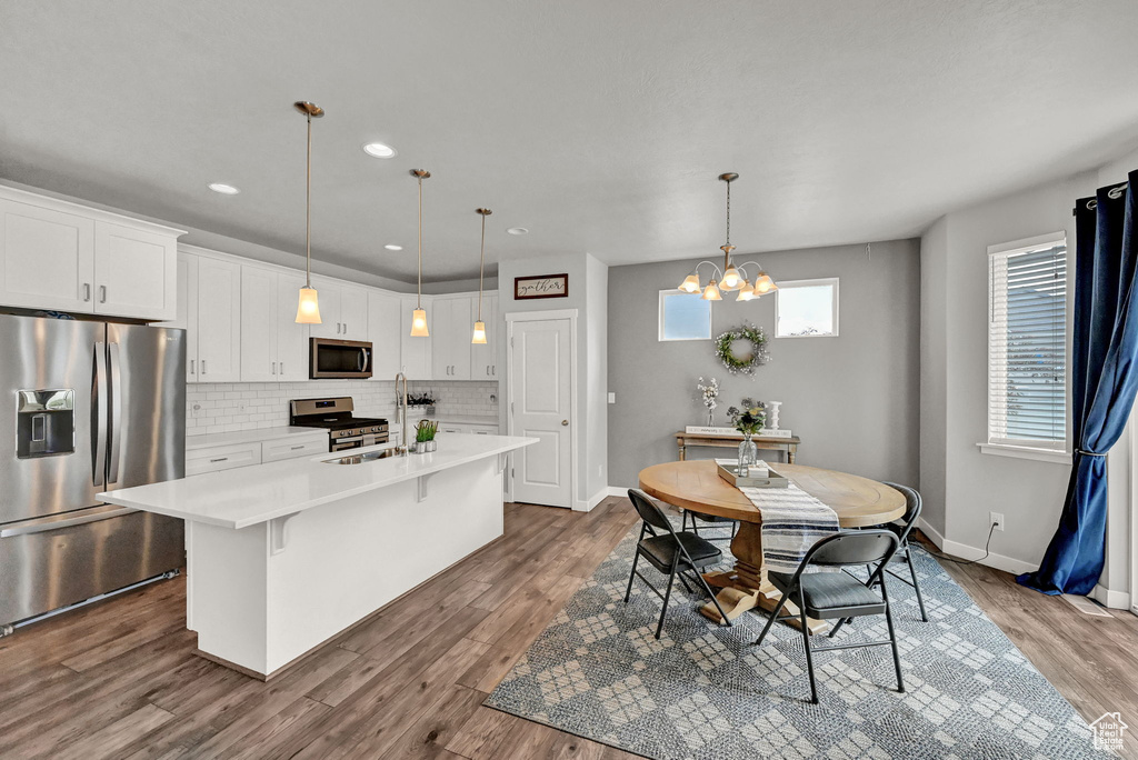 Kitchen featuring tasteful backsplash, hardwood / wood-style flooring, hanging light fixtures, white cabinets, and appliances with stainless steel finishes