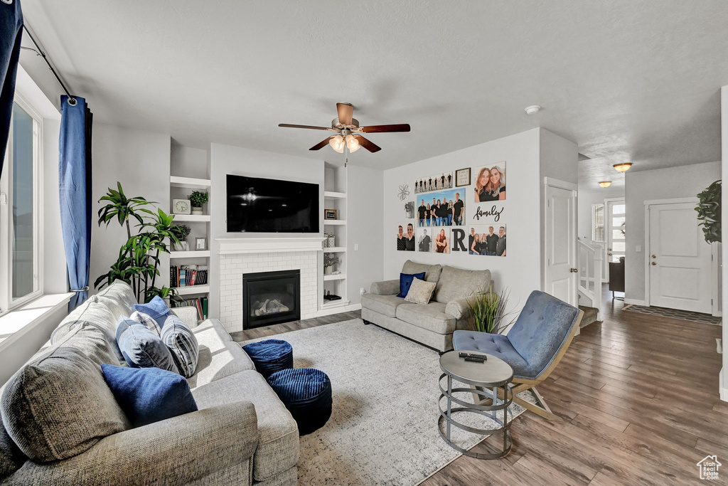 Living room featuring a fireplace, wood-type flooring, built in features, and ceiling fan