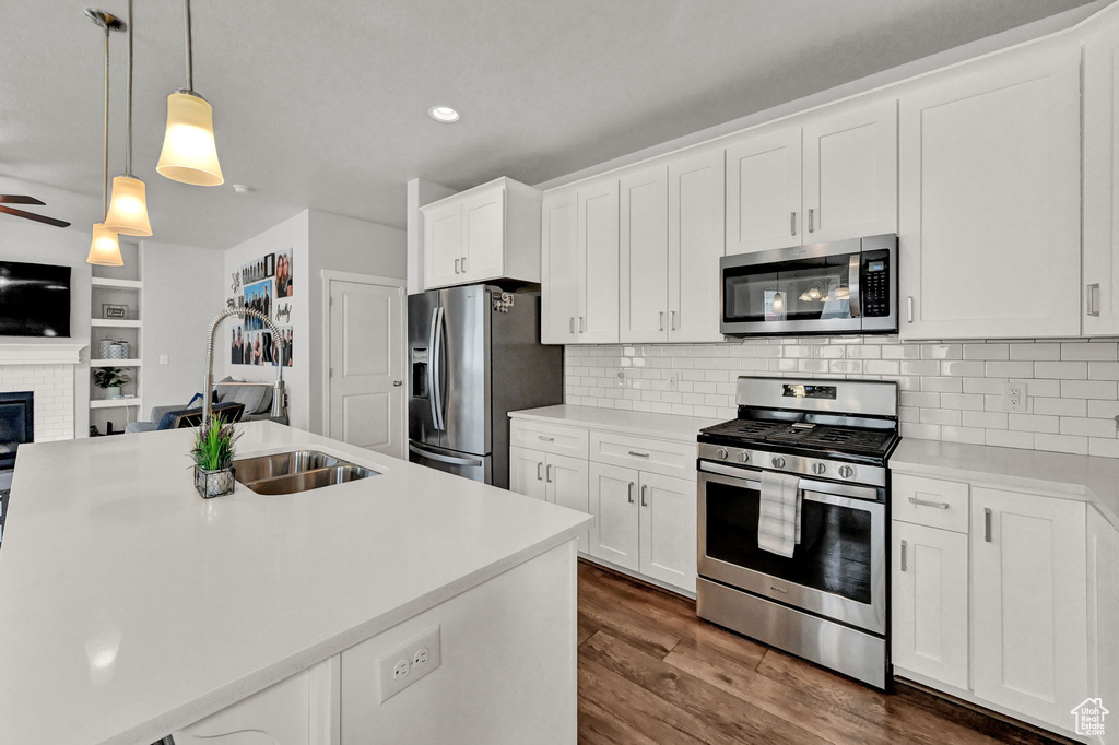 Kitchen with white cabinets, backsplash, dark wood-type flooring, stainless steel appliances, and a brick fireplace