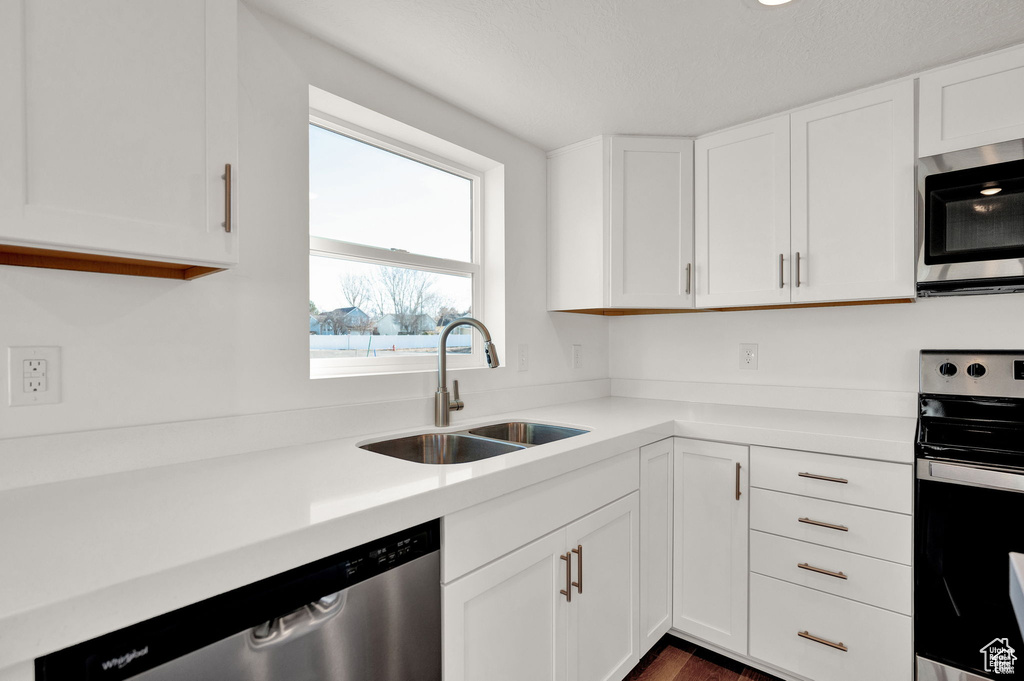 Kitchen with dark wood-type flooring, sink, white cabinets, and stainless steel appliances