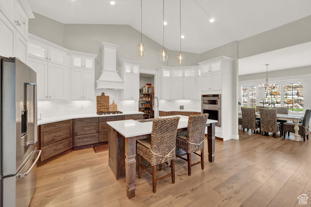 Kitchen featuring white cabinetry, tasteful backsplash, stainless steel appliances, and custom range hood