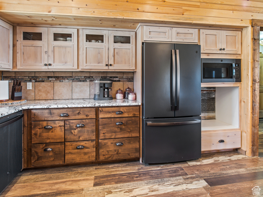 Kitchen featuring black appliances, decorative backsplash, hardwood / wood-style flooring, and light stone countertops