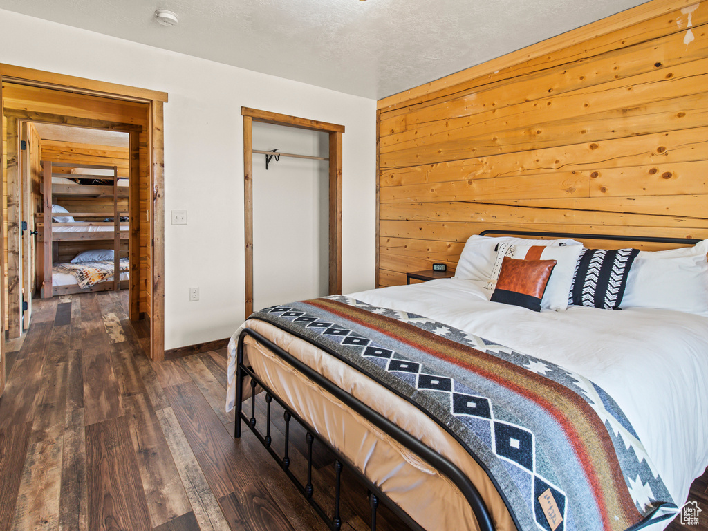 Bedroom with wood walls, a textured ceiling, a closet, and wood-type flooring