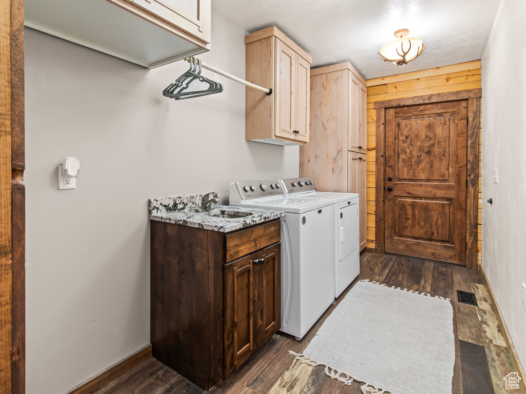 Laundry area featuring washer and clothes dryer, sink, cabinets, wood walls, and dark hardwood / wood-style flooring