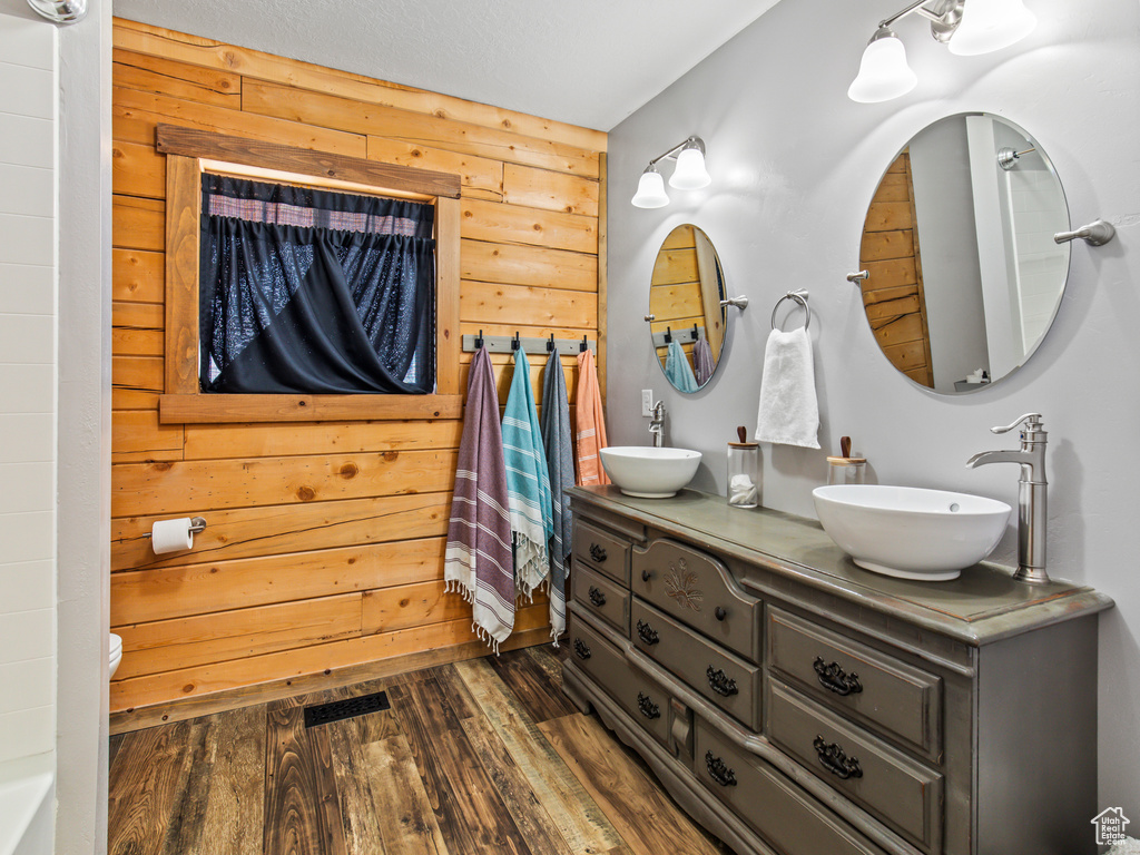 Bathroom with wood-type flooring, wood walls, and dual bowl vanity