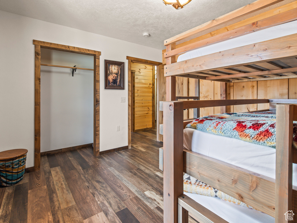 Bedroom featuring dark hardwood / wood-style floors, wood walls, a closet, and a textured ceiling