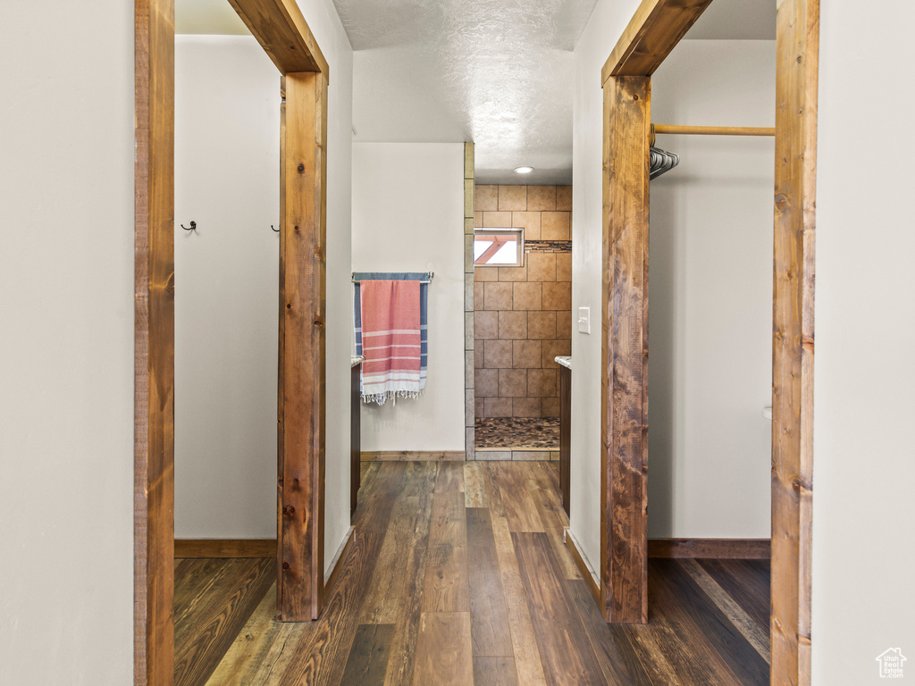 Hall featuring a textured ceiling, wood-type flooring, and tile walls