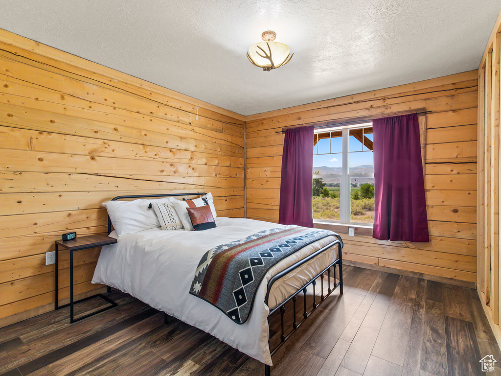 Bedroom with a textured ceiling, wooden walls, and dark wood-type flooring