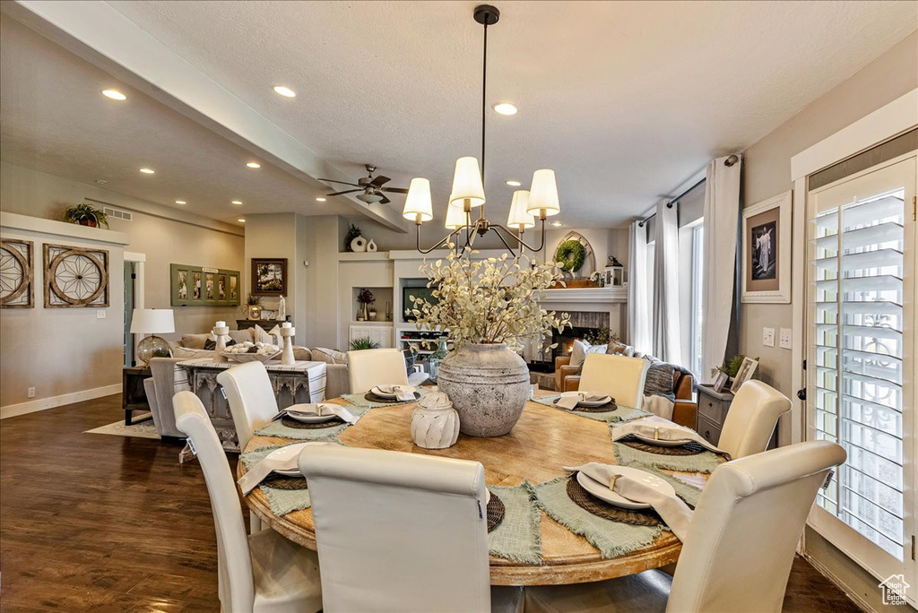 Dining space featuring dark wood-type flooring, ceiling fan with notable chandelier, and a wealth of natural light