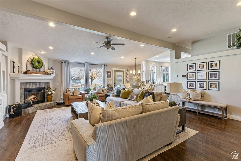 Living room featuring dark hardwood / wood-style floors, ceiling fan with notable chandelier, a fireplace, and a textured ceiling