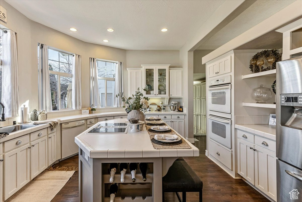 Kitchen with white cabinetry, white appliances, a center island, dark hardwood / wood-style flooring, and sink