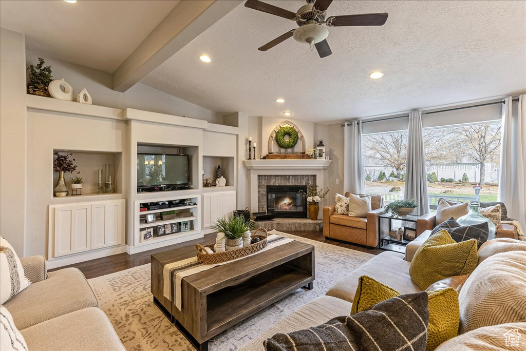 Living room featuring vaulted ceiling with beams, a textured ceiling, ceiling fan, a fireplace, and wood-type flooring