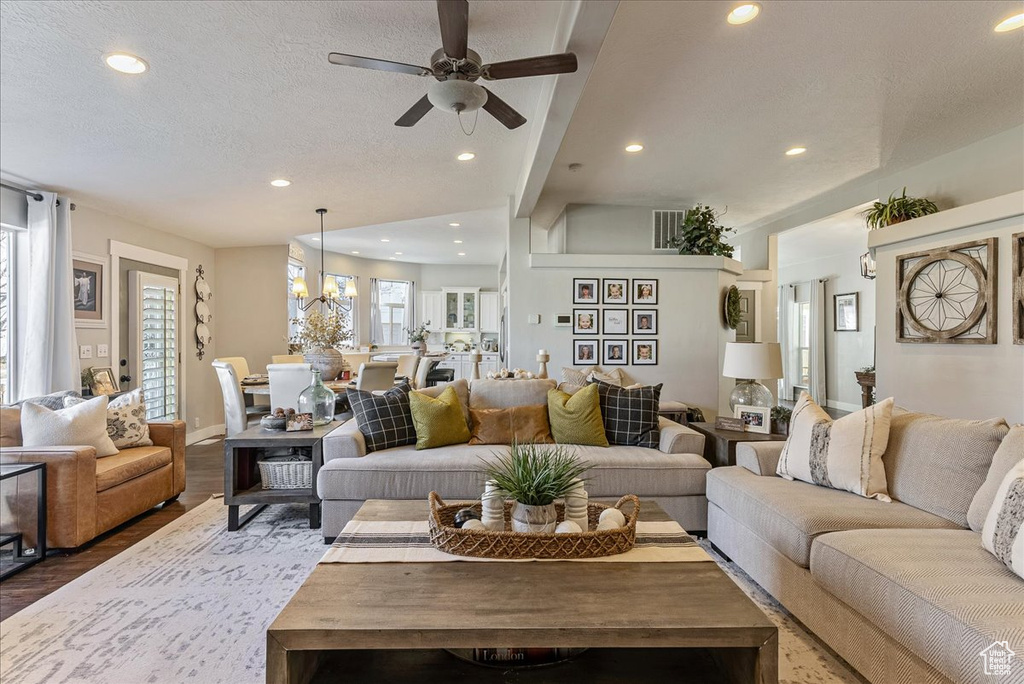 Living room with a textured ceiling, a wealth of natural light, ceiling fan, and dark wood-type flooring