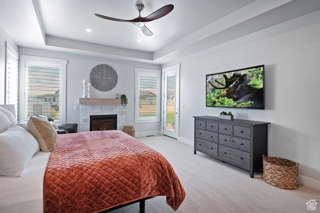 Bedroom with light carpet, a tiled fireplace, access to outside, and a raised ceiling