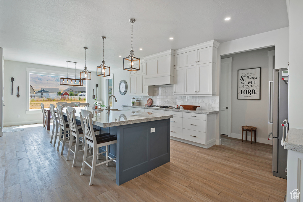 Kitchen with tasteful backsplash, a center island with sink, decorative light fixtures, light wood-type flooring, and white cabinetry