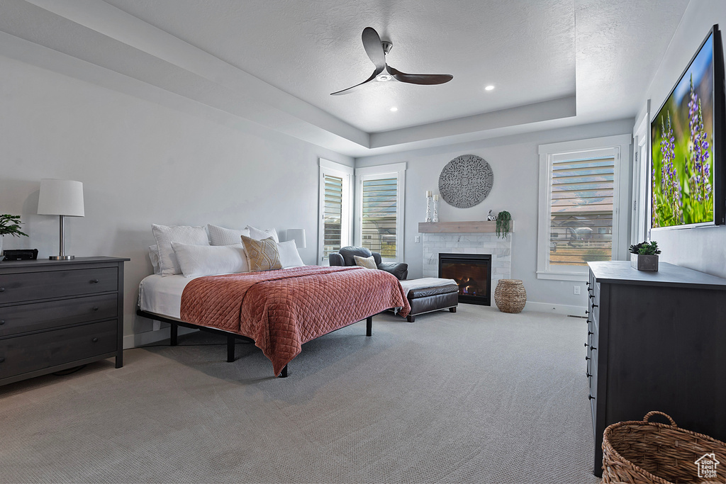 Bedroom featuring ceiling fan, light carpet, a tile fireplace, and a tray ceiling