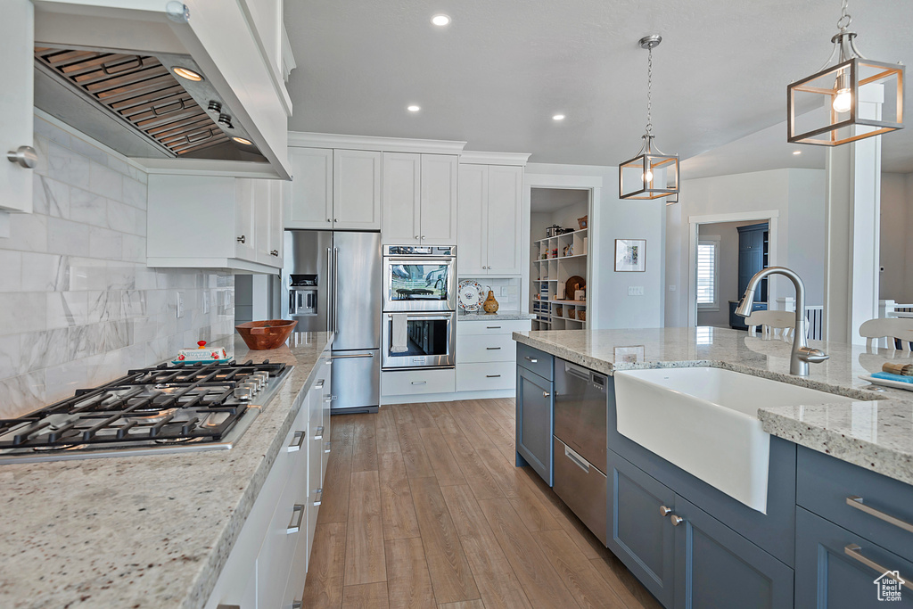 Kitchen with decorative light fixtures, wall chimney range hood, white cabinets, decorative backsplash, and light hardwood / wood-style floors