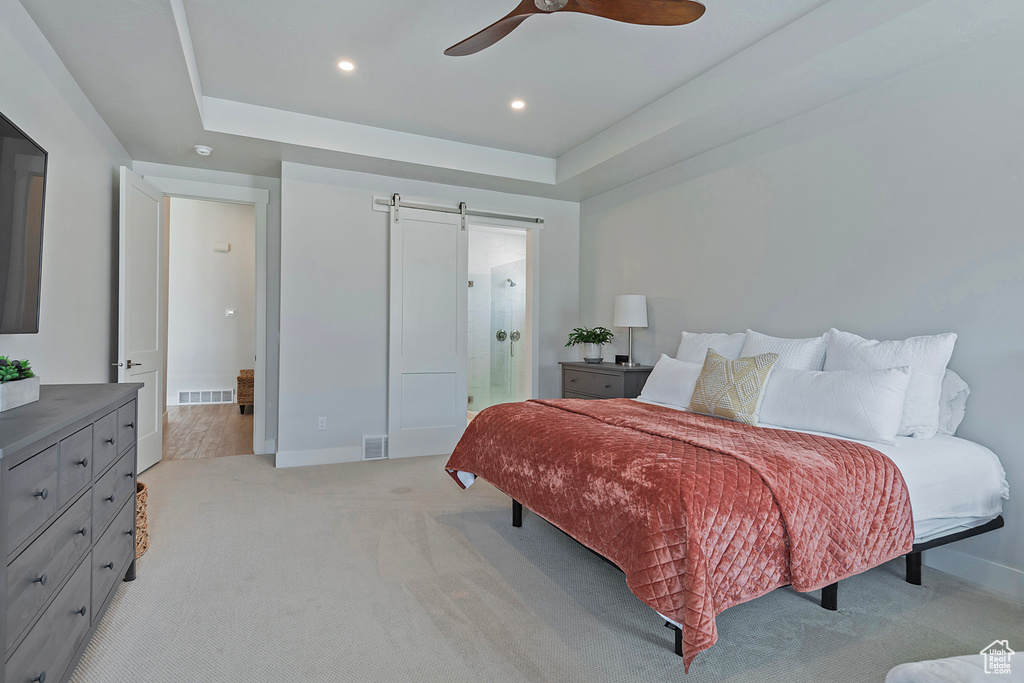 Carpeted bedroom with ensuite bath, ceiling fan, a tray ceiling, and a barn door