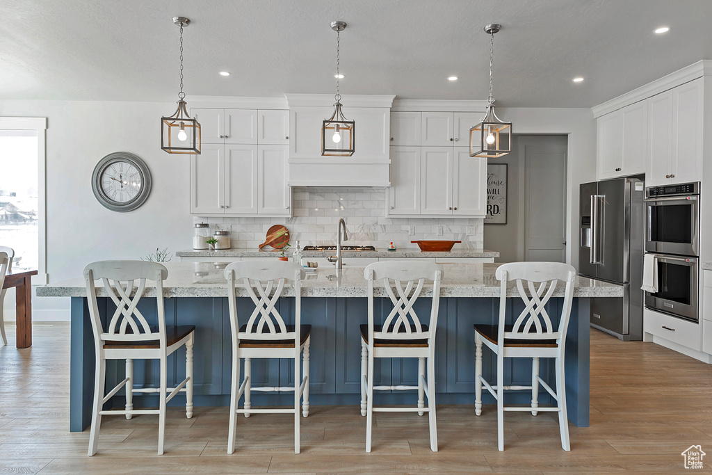 Kitchen featuring tasteful backsplash, stainless steel appliances, light hardwood / wood-style floors, hanging light fixtures, and a center island with sink