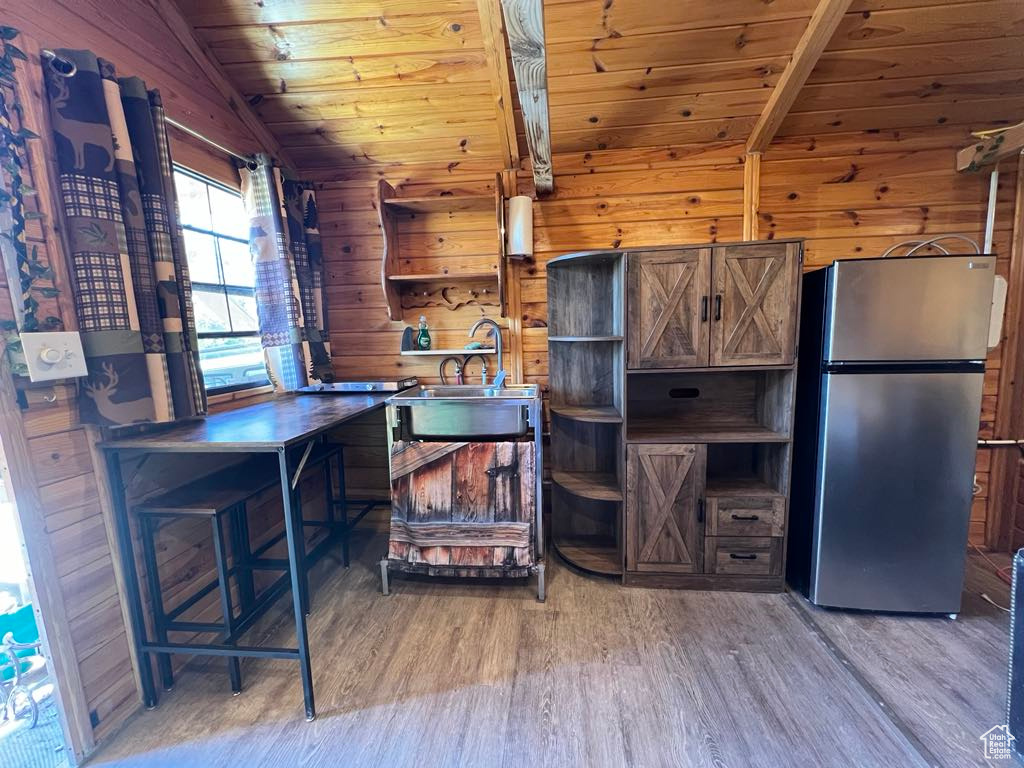 Kitchen featuring stainless steel counters, hardwood / wood-style floors, stainless steel fridge, lofted ceiling, and wood walls