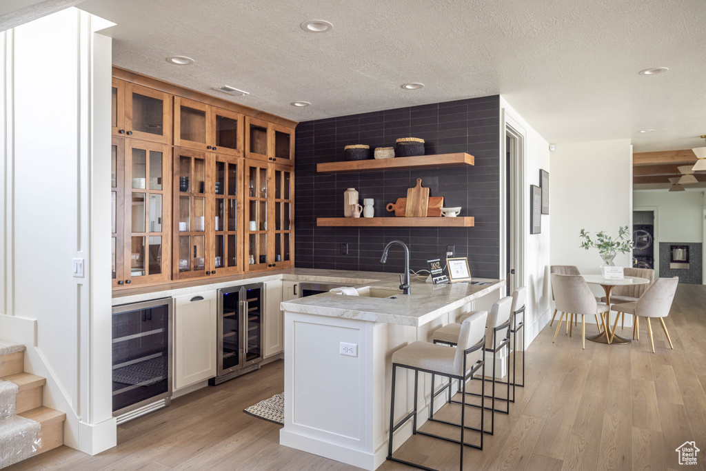 Interior space with white cabinets, beverage cooler, light hardwood / wood-style flooring, and tasteful backsplash