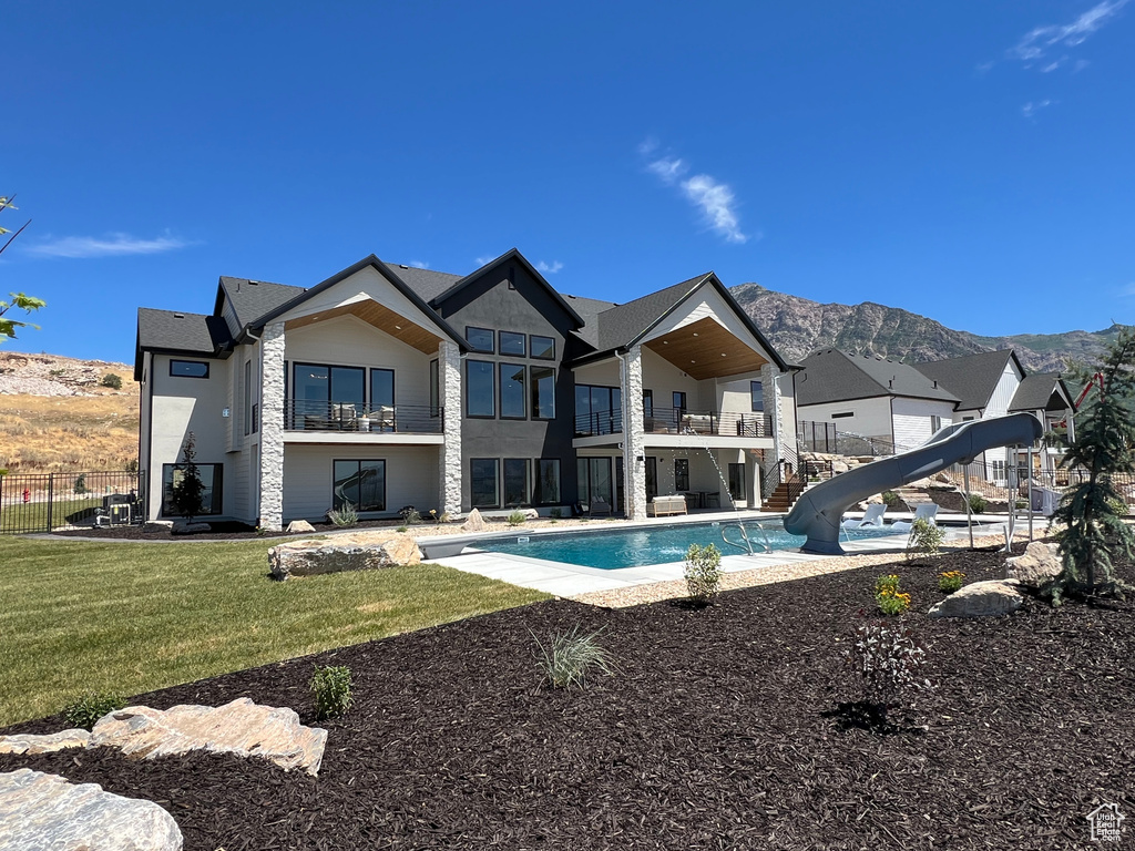 Back of property with a balcony, a mountain view, a fenced in pool, and a lawn