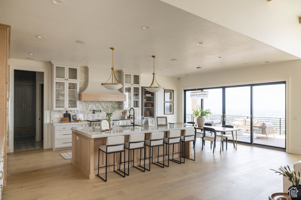 Kitchen featuring tasteful backsplash, hanging light fixtures, white cabinets, an island with sink, and a kitchen breakfast bar