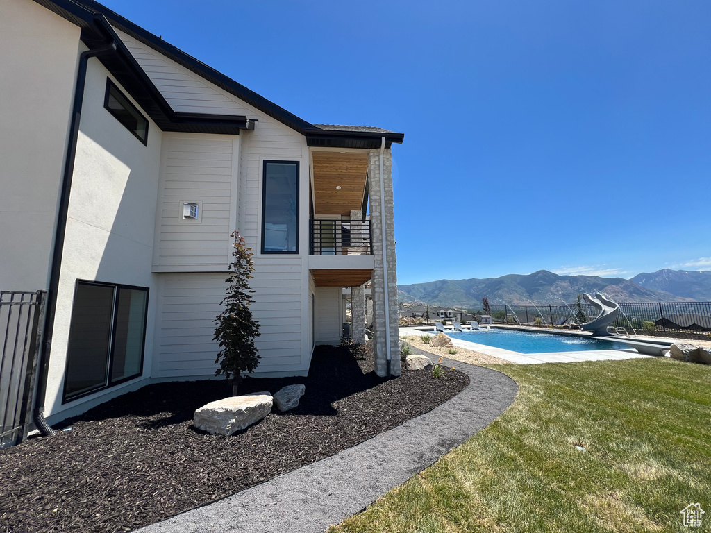 Rear view of property featuring a mountain view, a balcony, a lawn, and a fenced in pool