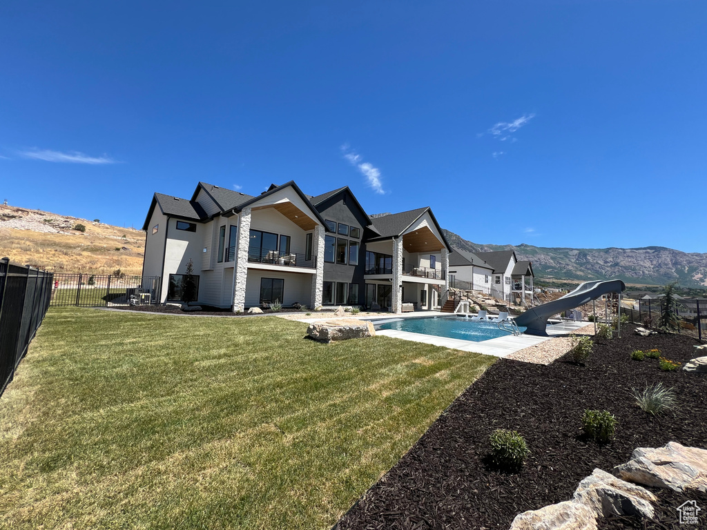 Back of house featuring a fenced in pool, a mountain view, a balcony, a patio area, and a yard