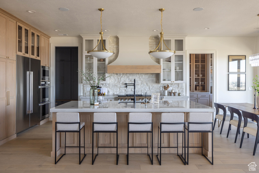 Kitchen with a breakfast bar area, custom range hood, light hardwood / wood-style flooring, backsplash, and an island with sink