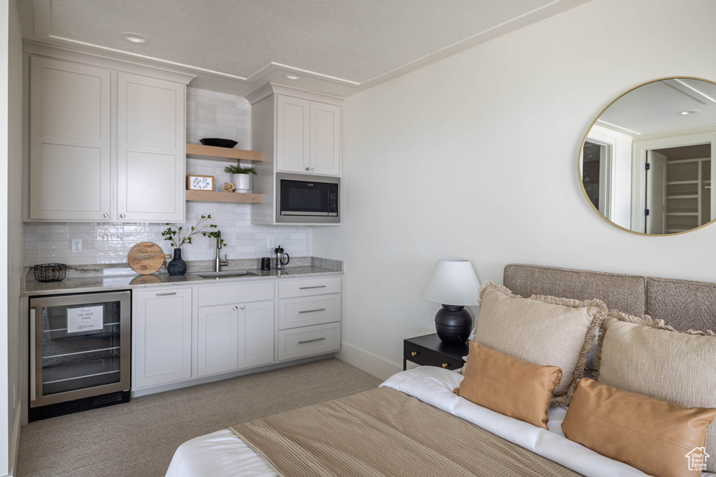 Interior space with decorative backsplash, sink, stainless steel microwave, light colored carpet, and wine cooler