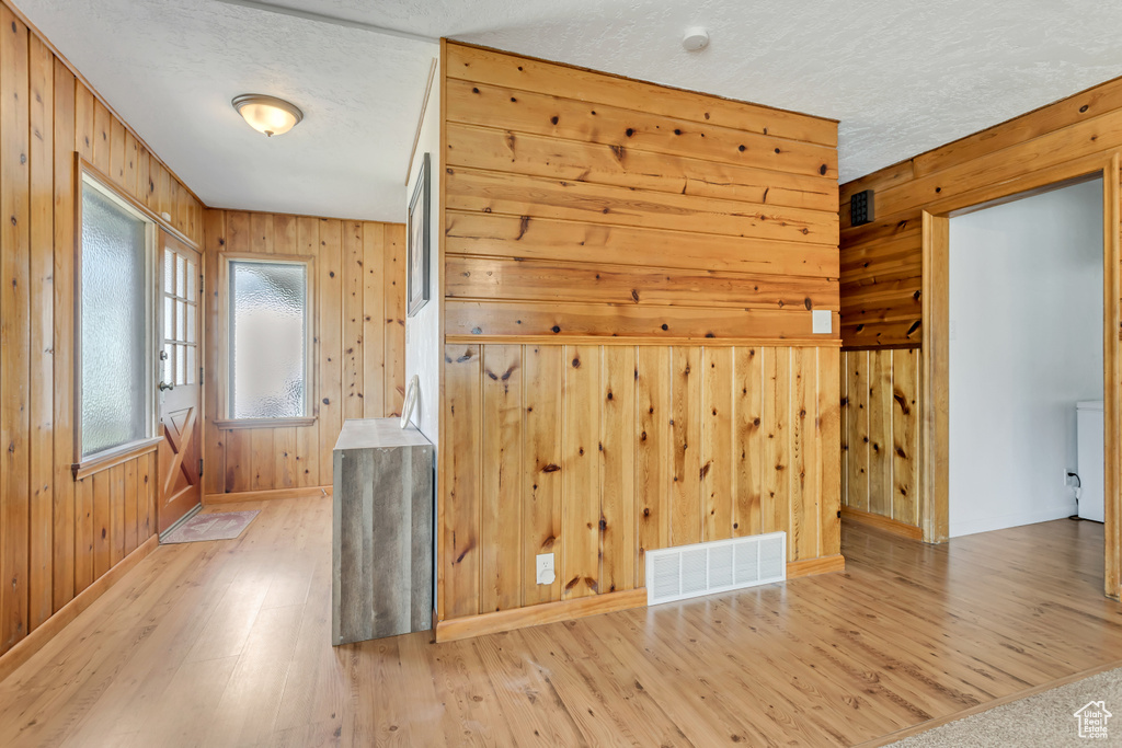 Spare room featuring light hardwood / wood-style floors, wooden walls, and a textured ceiling