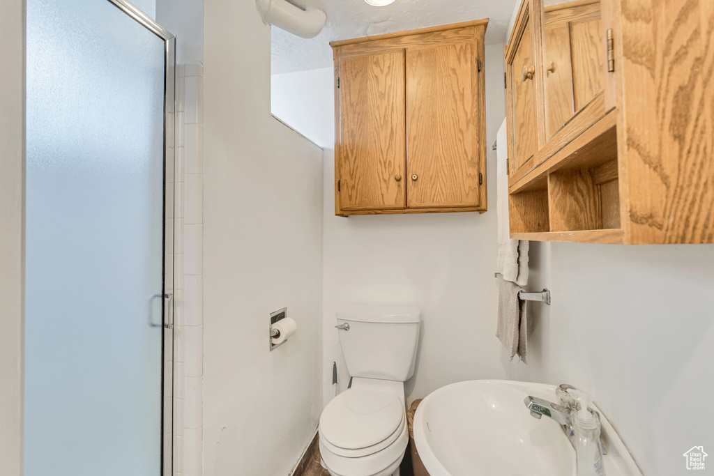 Bathroom featuring a shower with shower door, sink, and toilet