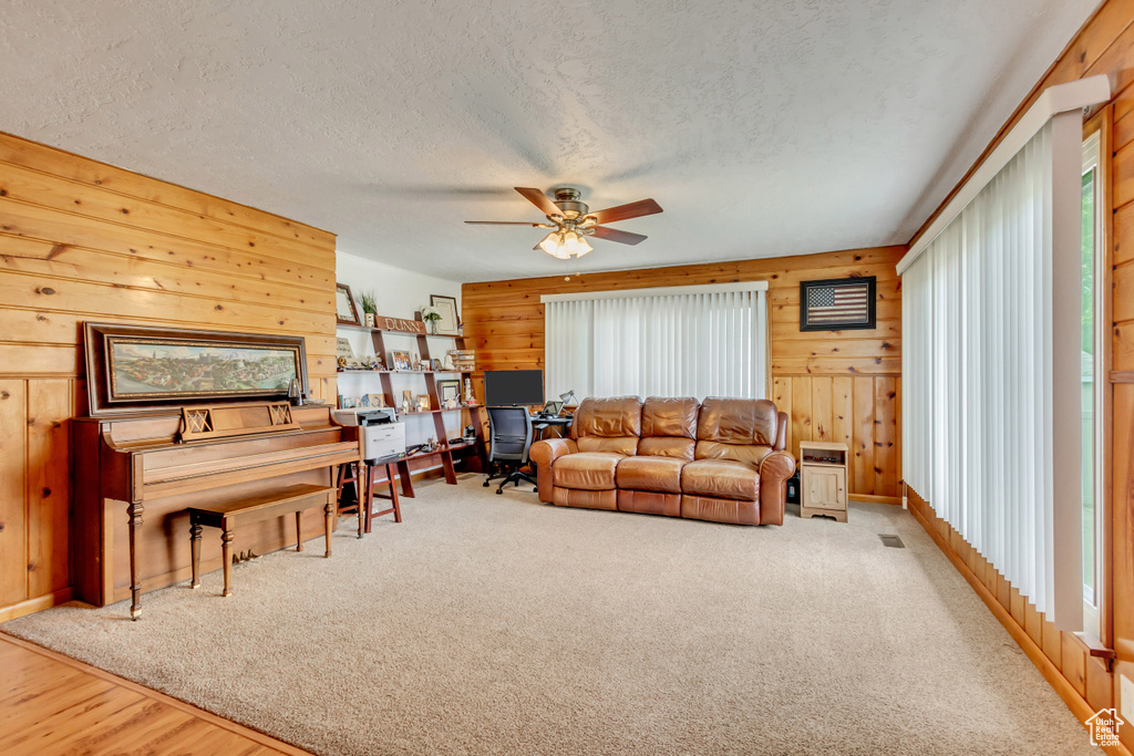 Carpeted living room with a textured ceiling, ceiling fan, and a healthy amount of sunlight