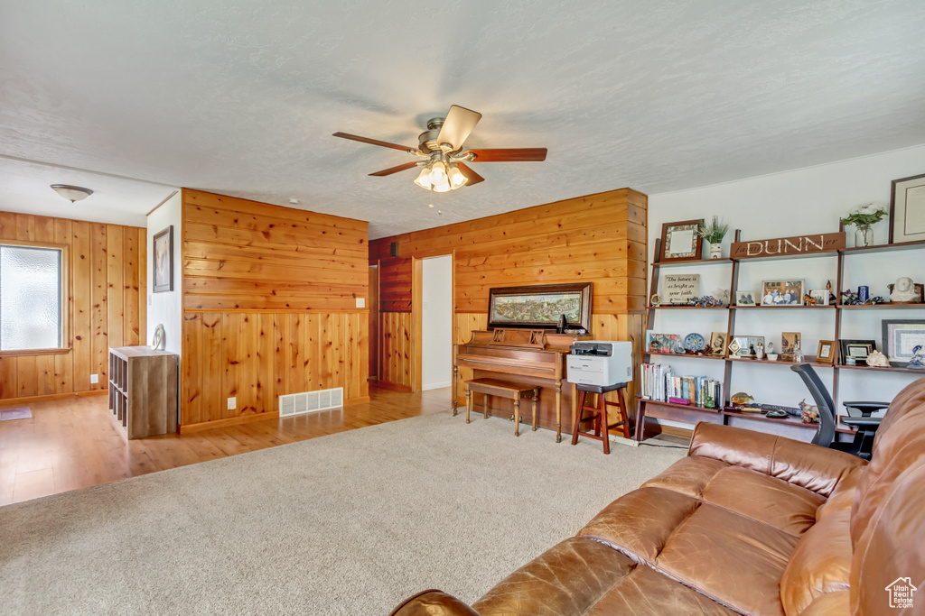 Living room with a textured ceiling, light hardwood / wood-style flooring, wooden walls, and ceiling fan