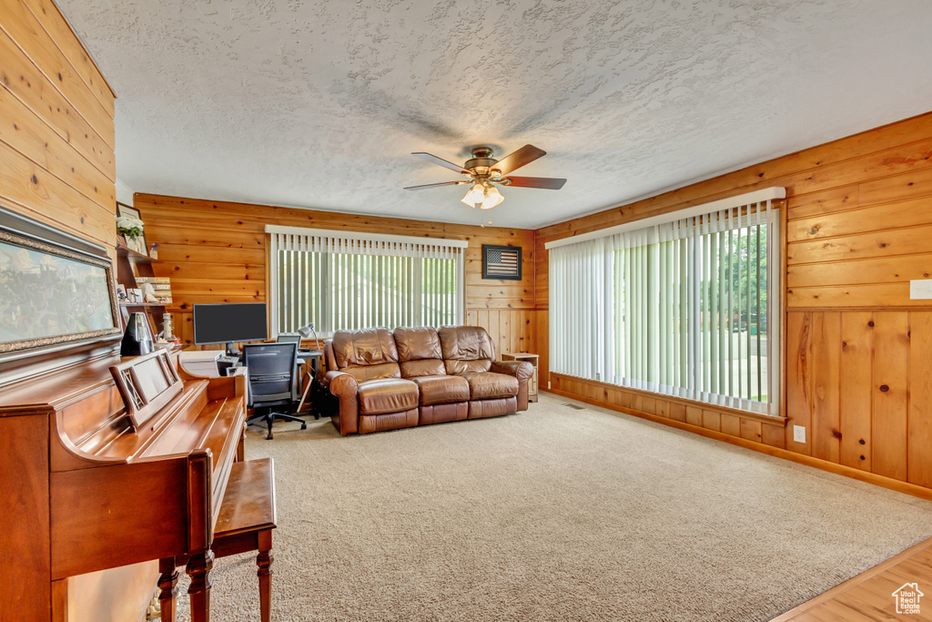 Carpeted living room with a textured ceiling, a healthy amount of sunlight, ceiling fan, and wooden walls